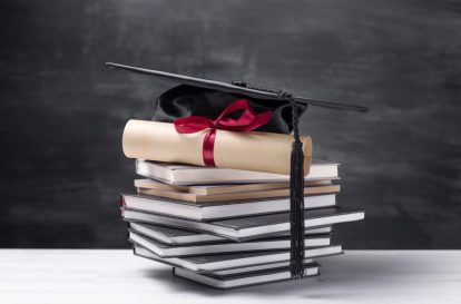 A stack of books with a graduation cap on top
